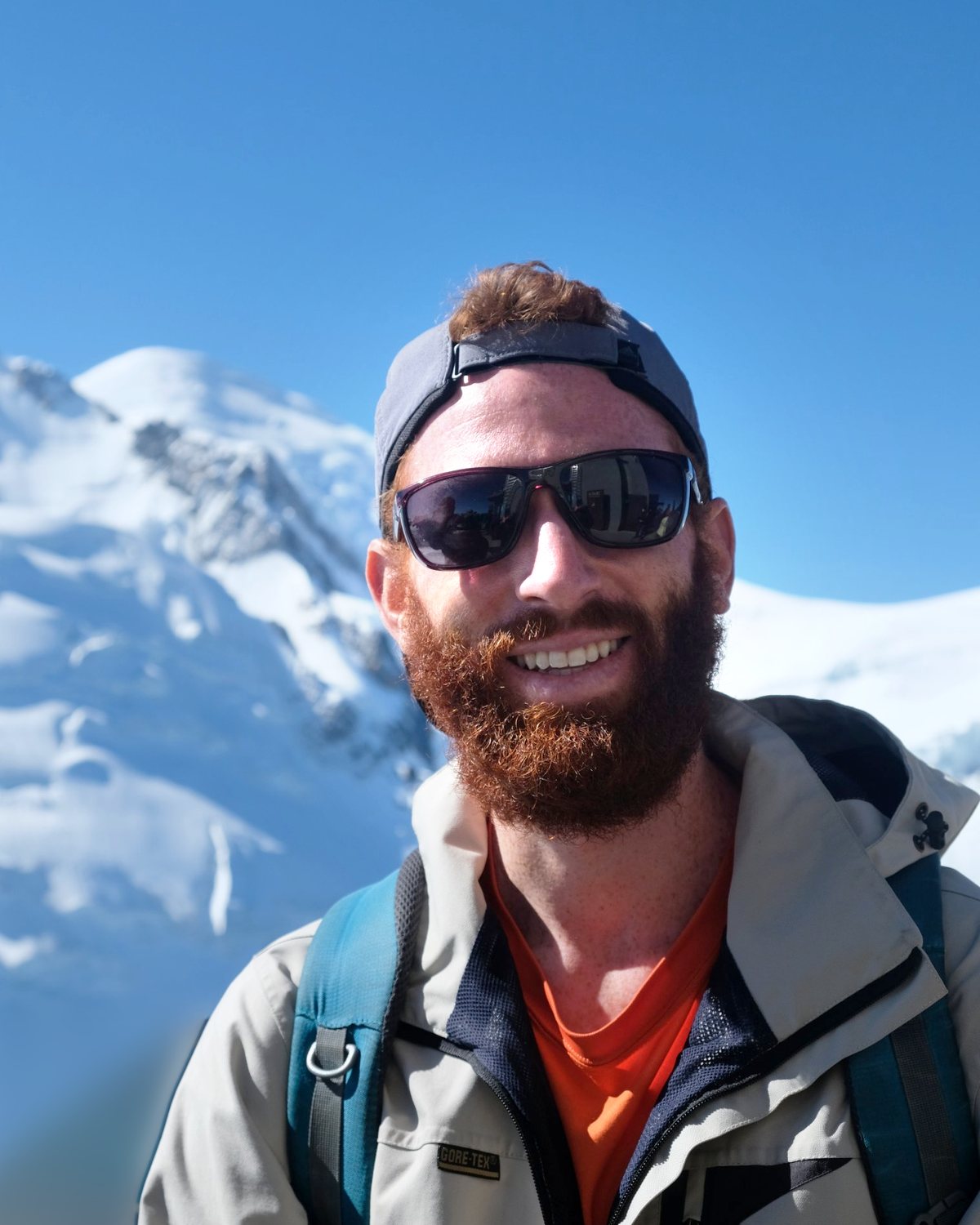 Jake Brockbank smiling in the Alps with a snowy peak behind him